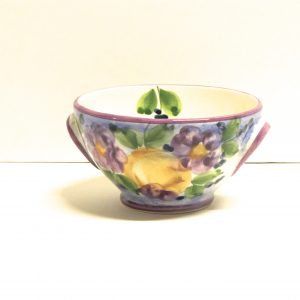 en keramik skål från lena linderholms kollektion viola den är målad för hand och dekorationen är violblommor målade i syrenlila nyanser med inslag av gröna blad och en ljusbrun vas där det sitter i violblommor i. inuti skålen finns en målad grön kvist.