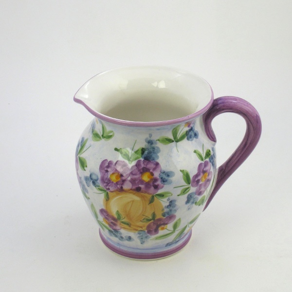 en keramik kanna från lena linderholms kollektion viola.kannan är vackert målad med violer på kannan som är målad i syrenlila med handtag i lila färg. den syrenlila färgen kommer tillbaka i överkant av kannan. handmålad.